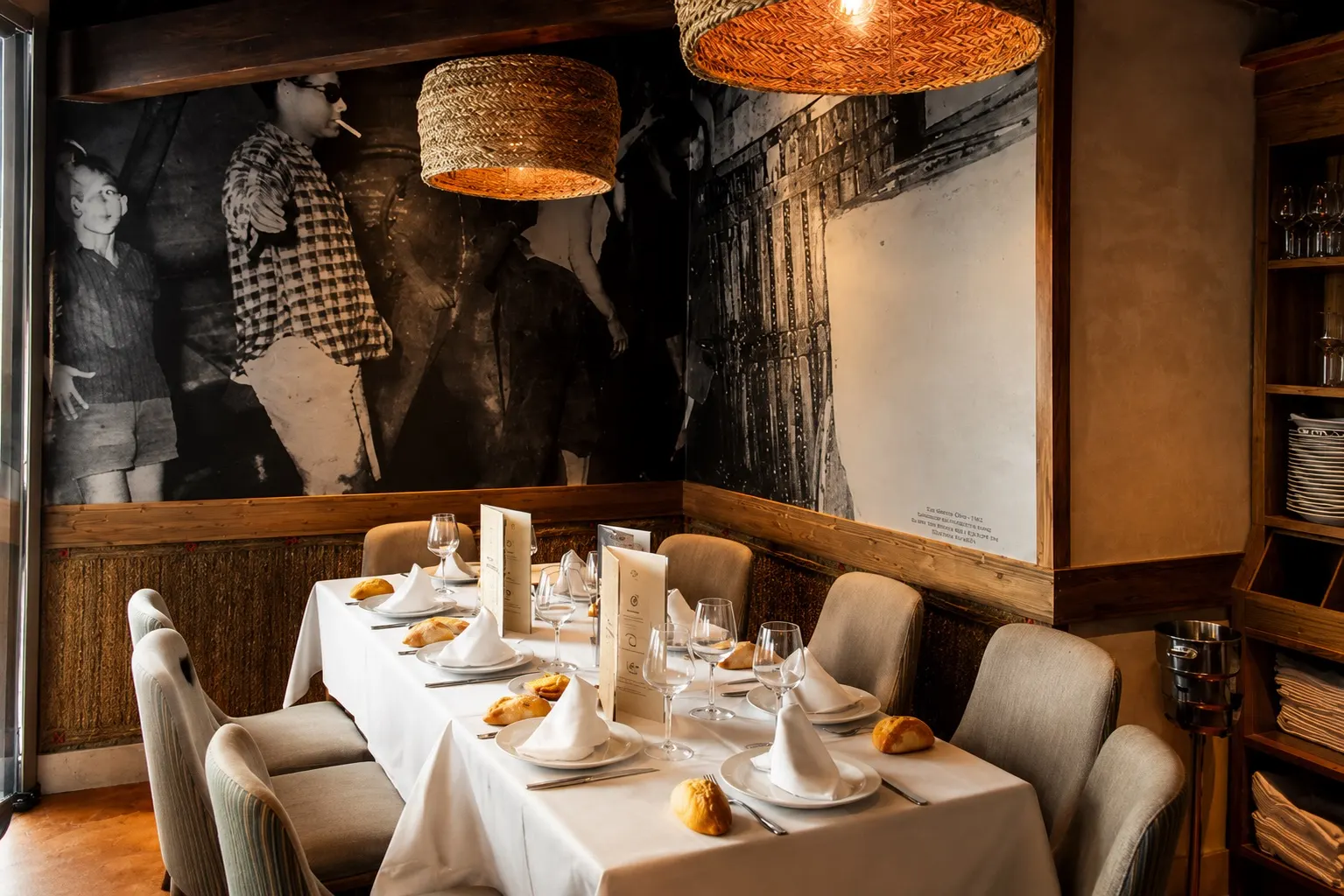 Rincón de la sala de El Garnacho: mural de la vendimia, lámparas de esparto y mesa vestida con mantel blanco